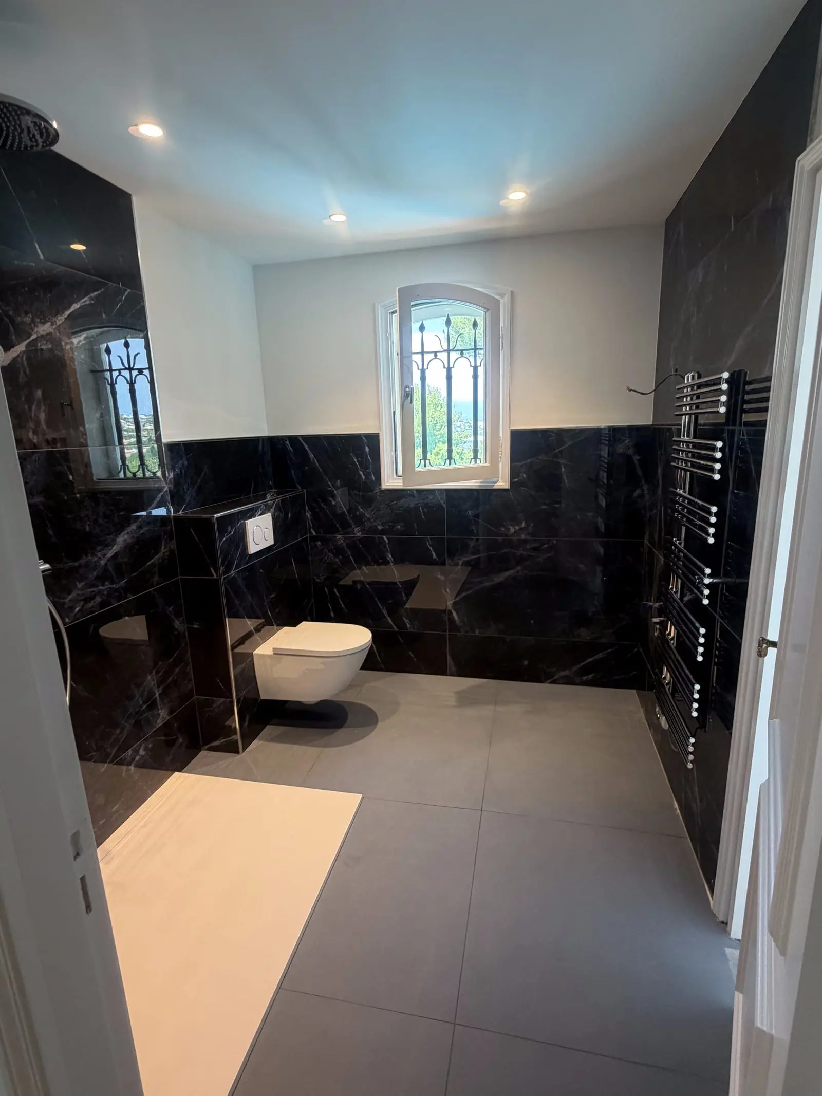 Salle de bain rénovée en marbre noir avec WC suspendu et sèche-serviettes par CMVR à Auribeau-sur-Siagne